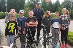 Zdjęcie przedstawiające policjanta stojącego wraz z dziećmi które egzaminował na kartę rowerową