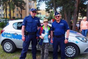 Zdjęcie przedstawiające policjantów stojących wraz z chłopcem uczestnikiem festynu