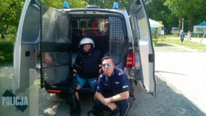 Zdjęcie przedstawiające policjanta wraz z chłopcem ubranym w policyjne oporządzenie stojących koło radiowozu