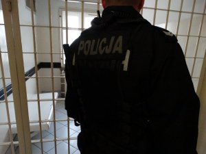 Zdjęcie przedstawiające policjanta stojącego przy kratach od pomieszczenia dla osób zatrzymanych