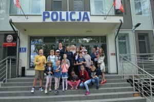 Zdjęcie przedstawiające policjantów wraz z dziećmi stojących przed budynkiem budynku komendy Policji