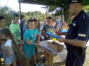 Zdjęcie przedstawiające policjanta rozdającego dzieciom opaski odblaskowe