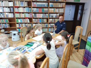 Zdjęcie przedstawiające policjanta na spotkaniu z dziećmi w bibliotece