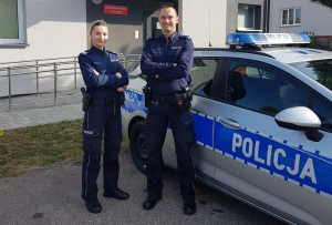 Zdjęcie przedstawiające dwójkę policjantów stojących koło radiowozu