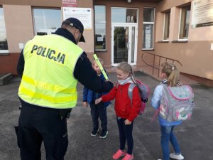 Zdjęcie przedstawiające policjanta przekazującego dzieciom elementy odblaskowe