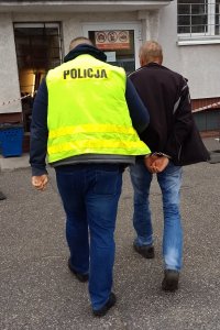 Zdjęcie przedstawiające policjanta prowadzącego osobę zatrzymaną