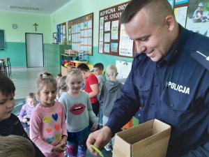 Zdjęcie przedstawiające policjanta podczas rozdawania dzieciom gadżetów odblaskowych