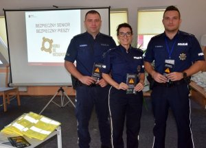 Zdjęcie przedstawiające trójkę policjantów trzymających w ręku ulotki