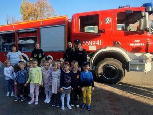 Zdjęcie przedstawiające policjantów stojących z dziećmi na przy wozie strażackim