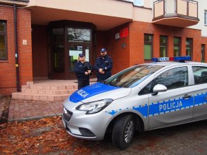 Zdjęcie przedstawiające dwójkę policjantów stojących obok radiowozu policyjnego