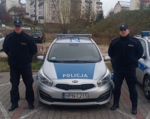 Zdjęcie przedstawiające policjantów stojących obok radiowozu