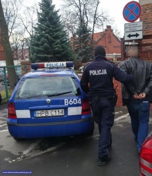 Zdjęcie przedstawiające policjanta prowadzącego osobę zatrzymaną