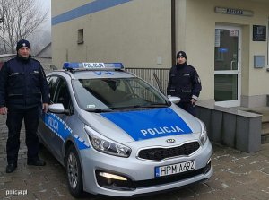 Zdjęcie przedstawiające dwójkę policjantów stojących przy radiowozie policyjnym