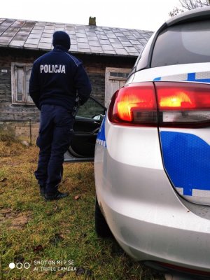 Zdjęcie przedstawiające policjanta stojącego obok radiowozu policyjnego