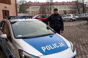 Zdjęcie przedstawiające policjanta stojącego obok radiowozu