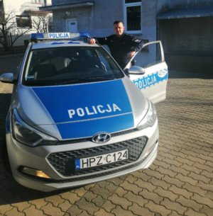 Zdjęcie przedstawiające policjanta stojącego przy radiowozie