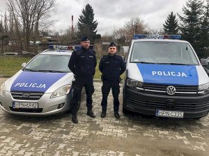 Zdjęcie przedstawiające dwójkę policjantów stojących koło oznakowanego radiowozu