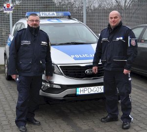 Zdjęcie przedstawiające dwójkę policjantów stojących przy radiowozie policyjnym