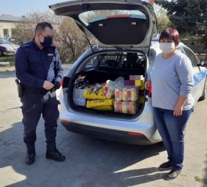 Zdjęcie przedstawiające policjanta oraz kobietę stojących przy bagażniku radiowozu, wypełnionym karmą dla zwierząt