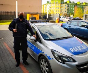 Zdjęcie przedstawiające policjanta stojącego obok radiowozu