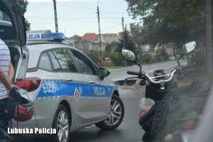 Zdjęcie przedstawiające oznakowany radiowóz policyjny ze stojącym obok niego motocyklem