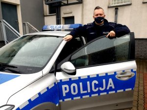 Zdjęcie przedstawiające policjanta stojącego przy radiowozie