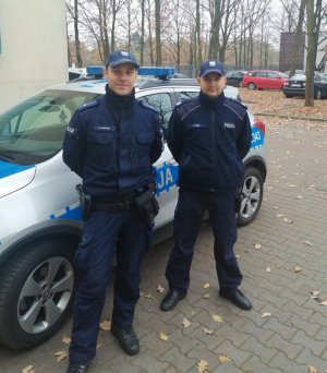 Zdjęcie przedstawiające dwójkę  umundurowanych policjantów stojących obok radiowozu
