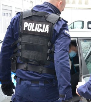 Zdjęcie przedstawiające policjanta stojącego koło radiowozu w którym siedzi zatrzymany mężczyzna