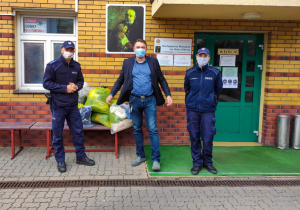 Zdjęcie przedstawiające dwójkę policjantów oraz mężczyznę, stojących przy workach foliowych z odzieżą