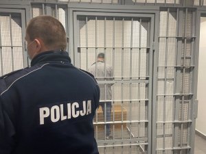 Zdjęcie przedstawiające policjanta stojącego przed wejściem dla pomieszczenia dla osób zatrzymanych