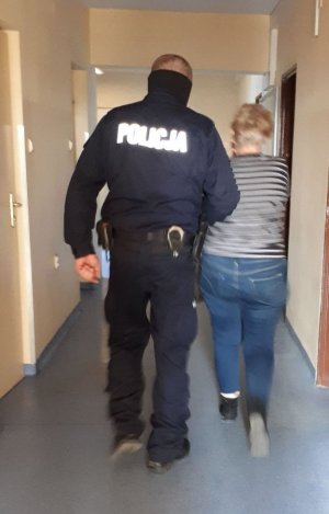 Zdjęcie przedstawiające policjanta prowadzącego osobę zatrzymaną