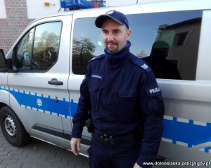 Zdjęcie przedstawiające policjanta stojącego przy radiowozie