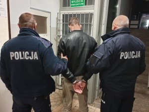 Zdjęcie przedstawiające dwójkę policjantów trzymających zatrzymanego skutego w kajdanki