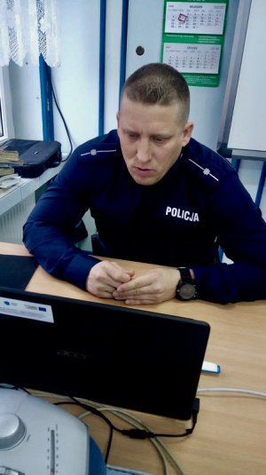 Zdjęcie przedstawiające policjanta siedzącego przy biurku