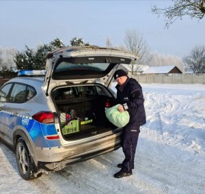 Zdjęcie przedstawiające policjanta stojącego wyciągającego z bagażnika radiowozu worek z żywnością