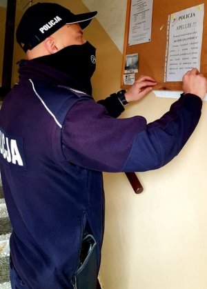Zdjęcie przedstawiające policjanta przyczepiającego do tablicy informacyjnej ulotkę