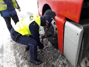 Zdjęcie przedstawiające policjanta odkręcającego koło od pojazdu ciężarowego