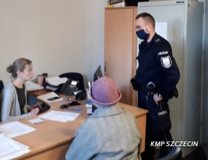 Zdjęcie przedstawiające policjanta  rozmawiającego z kobieta siedzącą przy biurku
