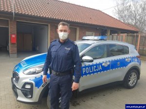 Zdjęcie przedstawiające policjanta stojącego obok radiowozu