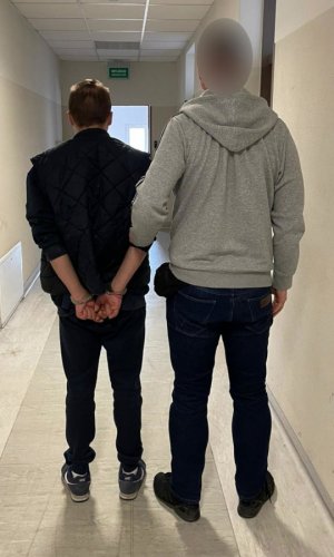 Zdjęcie przedstawiające dwójkę mężczyzn, z których jeden ma założone kajdanki na ręce trzymane z tyłu