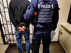 Zdjęcie przedstawiające policjanta stojącego z zatrzymanym skutym w kajdanki