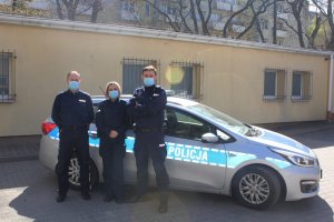 Zdjęcie przedstawiające trójkę policjantów stojących obok radiowozu