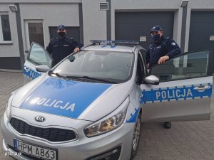 Zdjęcie przedstawiające policjantów stojących obok radiowozu