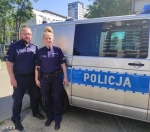 Zdjęcie przedstawiające dwójkę umundurowanych policjantów stojących obok radiowozu