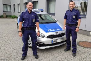 Zdjęcie przedstawiające dwójkę policjantów stojących obok radiowozu