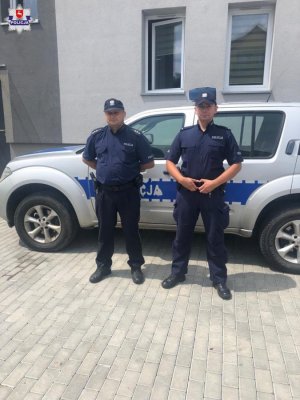 Zdjęcie przedstawiające dwójkę umundurowanych policjantów stojących obok radiowozu