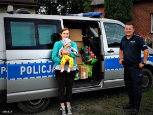 Zdjęcie przedstawiające policjanta stojącego z obok kobiety z dzieckiem na rekach