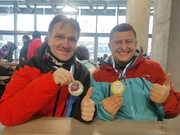 Zdjęcie dwóch uśmiechniętych mężczyzn ubranych w czerwone kurtki trzymających w ręku medale.