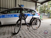 Zdjęcie blaszanego garażu wewnątrz, którego stoi rower oraz radiowóz policyjny.