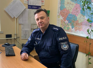 Zdjęcie umundurowanego policjanta w średnim wieku siedzącego przy biurku.